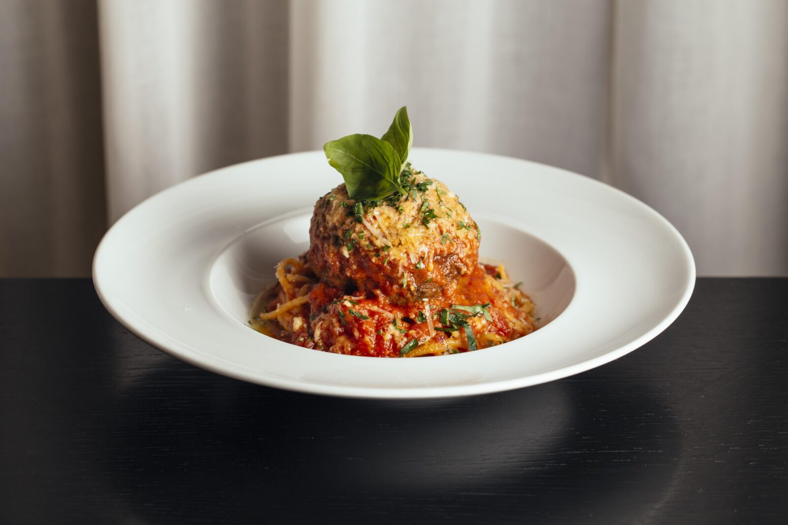 Spaghetti and meatballs in a white bowl with a leaf on the top.