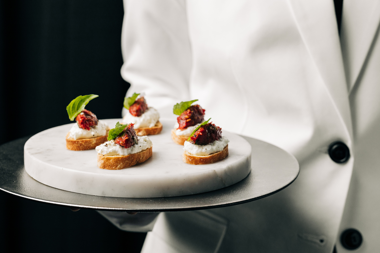 Tray of roasted tomato tartare served on a toasted baguette with stracciatella cheese and basil aioli. Topped with basil, olive oil, Maldon salt 