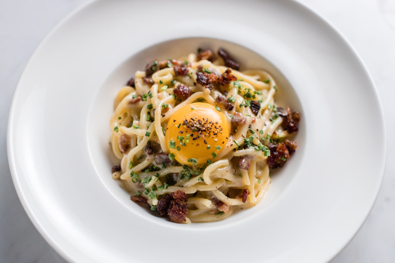 A bowl of spaghetti with an egg and small pieces of bacon.