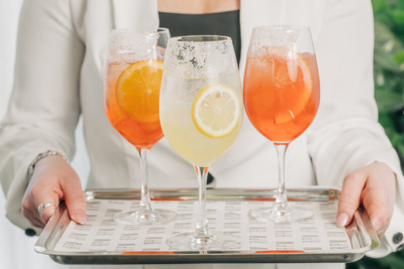 Server in white coat holding assorted spritz on tray.