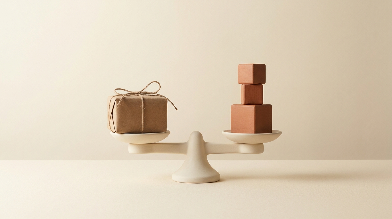 A kraft parcel balances against three terracotta blocks on a cream scale atop a warm ivory tabletop.