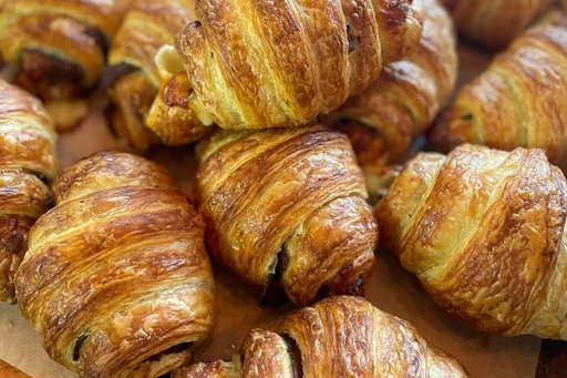 The island of Key Biscayne is lucky to have what we think is the best bakery in Miami. Technically it’s not a restaurant, but it’s home to our favorite croissants and sourdough bread. Luckily for you, Flour and Weirdoughs is the spot to come before the beach with your friends or family on the weekends too.
It’s also a great place to work from. There’s indoor seating and it’s pretty quiet during weekdays, after the morning rush. So, if you live in Brickell, you work from home and need a break from your apartment. Cross the bridge, you’ll be in bakery heaven in 10 to 15 minutes.
Flour and Weirdoughs is a rustic bakery that mills its flour in-house. All their sourdough breads are organic and filled with nutrients. If you’re looking for a ready-to-go breakfast item, we’d go for their eggs deep Danish with eggs, bacon, and cheese; a simple basic AF croissant (yes, that’s the name), ham and cheese croissant, or their famous It’s brisket b*tch croissant named after Britney Spears that comes with provolone, grain mustard, cured brisket (they cure it in-house for 11 days). You’ll never miss Paris again… Ok, you will but not for the croissants.