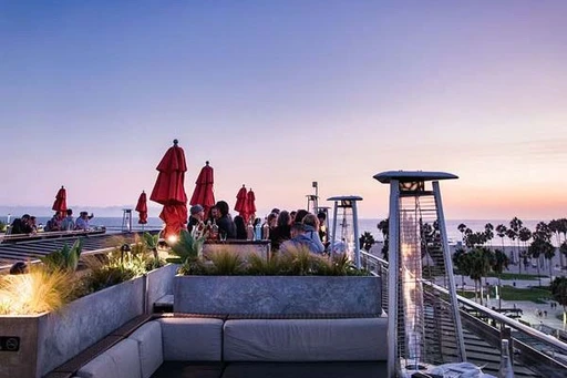 High Rooftop Lounge at Hotel Erwin 🌟
Beachside rooftop bar with chill vibes and epic sunsets.
From the roof terrace at the lovely Hotel Erwin rooftop bar, you get some amazing views over the Pacific Ocean and Venice Beach.
Being the only rooftop in Venice, High Rooftop Lounge feels a lot like a continuing of the beach below, with lounge sofas and large umbrellas. The only difference might be that up here you also have infrared (and blankets) keeping the heat up on chilly nights.
The rooftop bar offers a good selection of well made specialty cocktails and different Californian beers, along with some really tasty bar bites and a weekend brunch. The menu even includes sun screen, so visits during sunny days is no problem at all.
Expect a great lounge vibe on the terrace, perfect for relaxing drinks in the sun. And at night, there are often live DJs picking up the pace a notch.