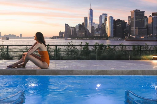 Just a short ferry ride from Manhattan, QC New York Spa on Governors Island offers a tranquil escape with stunning views of the city skyline and a wide array of luxurious wellness experiences.
Nestled in meticulously restored historic army barrack buildings, QC New York Spa combines the charm of 18th-century architecture with modern amenities. Visitors can explore labyrinth-like interiors adorned with elegant Italian furniture, art fixtures, and cozy relaxation areas, making it a unique blend of old-world charm and contemporary luxury.
The spa features over 20 wellness experiences, including themed saunas, steam rooms, and relaxation rooms. Highlights include the “Spa and the City” sauna with its New York skyline décor, the lavender-scented “Park Sauna,” and various foot baths and Vichy showers. The outdoor infinity pools, complete with hydro massage seats and loungers, offer breathtaking views of lower Manhattan and the Brooklyn Bridge, providing a serene contrast to the city’s hustle and bustle.