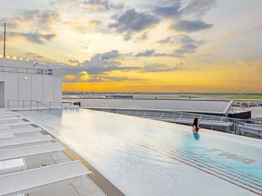 The TWA Hotel at JFK Airport offers an infinity pool that is different from all other rooftop pools NYC (and most other rooftop pools in the world). 

Called a 'rooftop pool-cuzzi', the pool is heated up to 95 degrees farenheit daily during the colder months. So it is open and available year-round, offering a much-needed respite during hot summer days, and warming swims in winter.

While lounging in the rooftop infinity pool or in one of the sun beds, you can enjoy thrilling views over JFK’s bustling Runway 4 Left/22 Right. Not your ordinary rooftop view.

Inspired by the infinity edge pool at the Hotel du Cap-Eden-Roc in Cap d’Antibes, France, the TWA Hotel rooftop pool is open daily from 7am to 11pm. Early morning, it is exclusive for guests staying at the hotel, but from 11am, anyone can make a reservation. For $25 Mon-Thu and $50 Fri-Sun you can enjoy the pool, observation deck and pool bar.