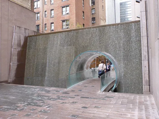 Have you ever walked through the Midtown Manhattan Waterfall?
Tucked into a small pocket park between buildings, you’ll find this gorgeous waterfall pathway.
The water feature is 20 feet tall and 40 feet wide, and is partially housed in plexiglass. The 17 foot-long glass tunnel runs beneath the waterfall, creating a water covered tubular path.
The sound from the water is soothing, and walking through the tube is exciting, especially for kids. (Bonus: the tube makes it easy to walk between 48th and 49th streets quickly!).
Only a block from Times Square’s bustling traffic, it’s a calming escape in the middle of Midtown Manhattan.
PRICE: 🎟Free & Open to the Public