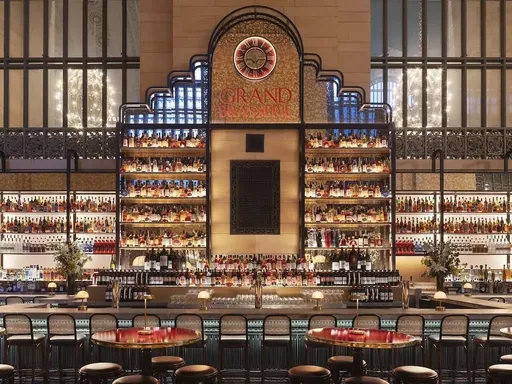Grand Central Terminal gains a massive French brasserie!
However, this historic landmark has given us plenty of reasons to bide our time there...
This month, the terminal gained another tenant, sure to ease the trials of traveling with its Parisian charms. Grand Brasserie took over the former City Winery space on October 8. Designed by the Rockwell Group, it seamlessly blends into the historic architecture of Vanderbilt Hall and mimics the various sidewalk cafes found in Paris—the front of the restaurant welcomes with towering greenery and black and white bistro chairs.
Passing through the wrought iron bar entryway, the main dining room houses red leather banquettes and enough chairs to seat a staggering 300 souls. As if that wasn’t enough, the 100-seat Green Room is decorated with black and white photos of New York’s past and features a grand marble bar with bottles that climb up to the ceiling.