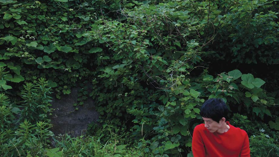 Ryo sat beside bushes outside - he wears a red Dior Homme knitted jumper