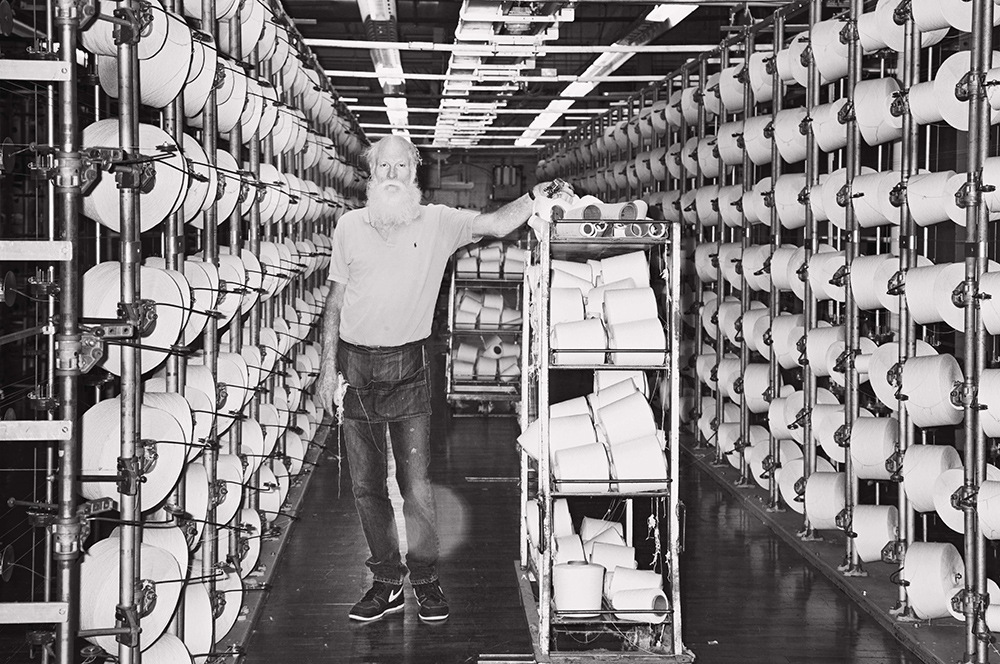 George Westmoreland, known as “Red”, loads yarn packages in the creel of a modern day warper at White Oak Mill, Greensboro