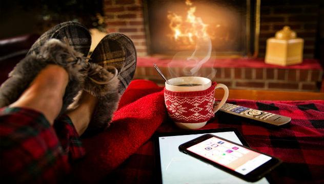 person with their feet up on front of a cozy fire with a hot drink