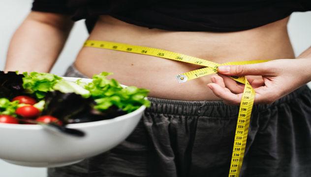 person measuring their waist holding a bowl of salad