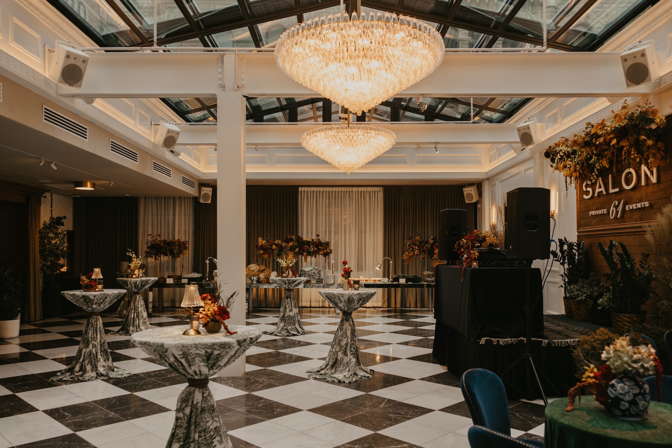 an open event space with hight ceilings, 2 large chandeliers and high top tables scattered through the room