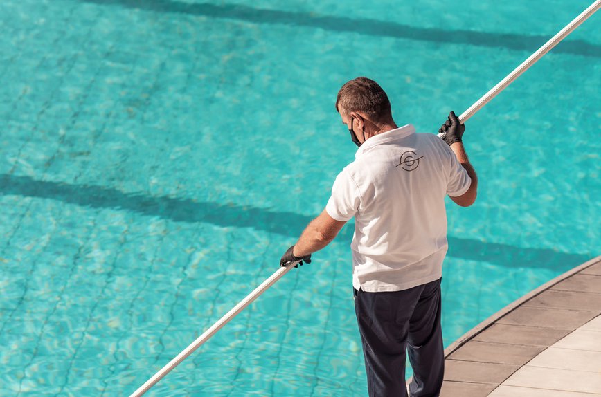 Employee cleaning the pool wearing mask and gloves