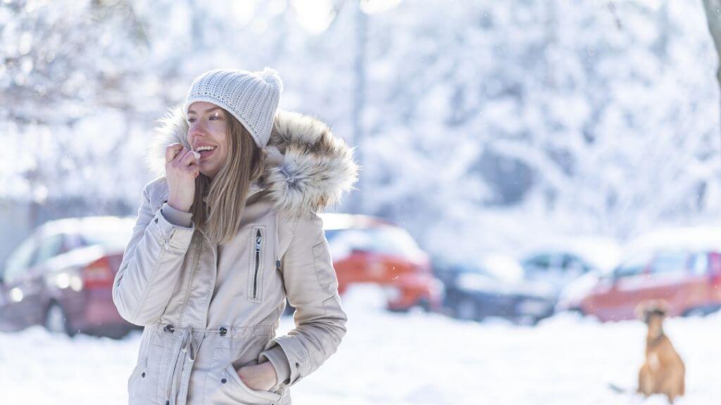 A woman in the snow applies moisturizer to her lips