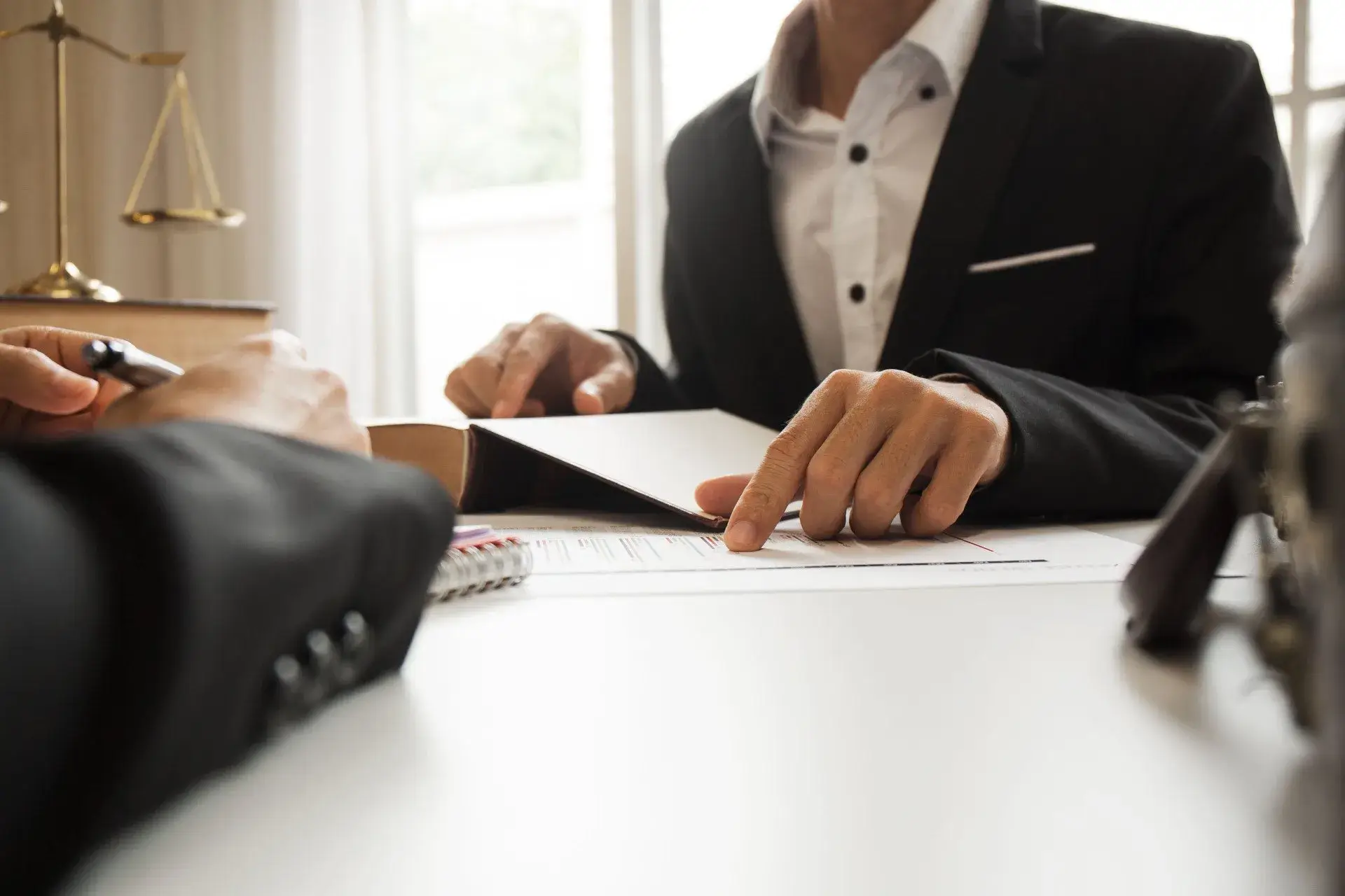 An attorney reviews and signs a document, then gestures to a key section, guiding the client through the details before they sign.