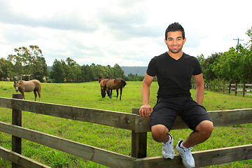 Image showing man sitting on fence of a horse paddock