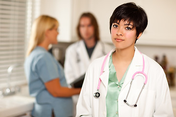 Image showing Pretty Latino Doctor Smiles at Camera as Colleagues Talk