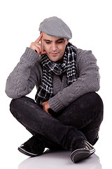 Image showing Portrait of a young man sitting on the floor, thinking and looking down, in autumn/winter clothes