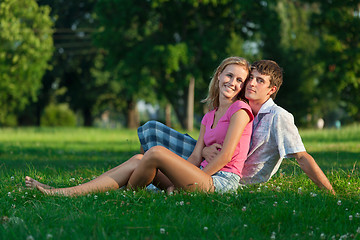 Image showing Two young lovers sitting on the lawn in the park and looks into 