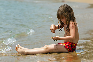 Image showing The little girl is sitting on a beach in the waves