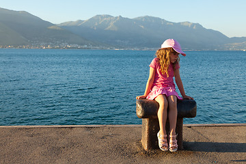 Image showing The little girl in a pink dress sitting on a bollard in the mari