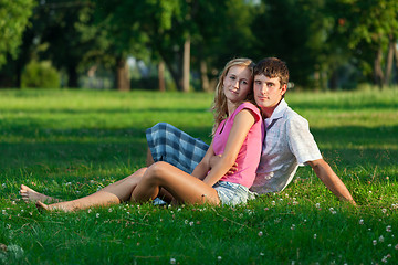 Image showing Two young lovers sitting on the lawn in the park and looks into 