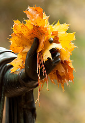 Image showing A bouquet of yellow autumn leaves in the hands of a bronze statu