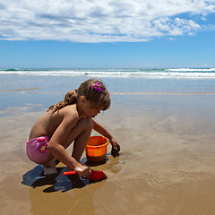 Image showing A girl playing on the wet sand with a shovel and pail