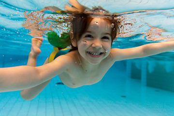 Image showing The girl smiles, swimming under water in the pool