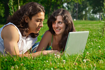 Image showing The boy and girl lying on the grass in the park with a laptop