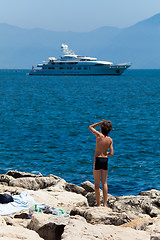 Image showing A boy on a brick bank admires luxury white yacht