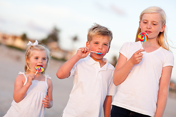 Image showing Cute Brother and Sisters Enjoying Their Lollipops Outside