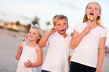 Image showing Cute Brother and Sisters Enjoying Their Lollipops Outside