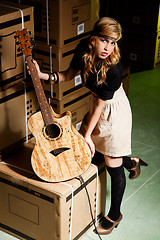 Image showing beautiful young woman with a classical guitar in a warehouse with boxes like scenario