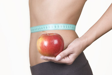 Image showing woman holding an red apple while measuring her waist