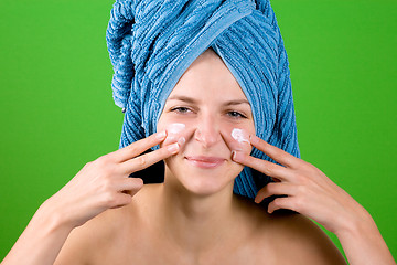 Image showing young woman in blue towel applying facial cream