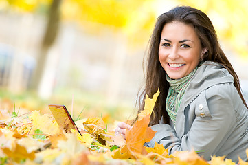 Image showing Happy student girl lying in autumn leaves with netbook