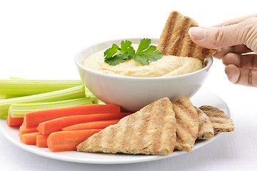 Image showing Hand dipping pita in hummus