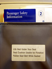 Image showing Inside a commercial airliner.  Shows the Safety Information brochures and barf bag in the seat pocket behind the airline seat in front of you.