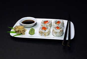 Image showing A California Roll (sushi) sliced on a dish with soy sauce, ginger, wasabi, and chopsticks.(14MP camera)