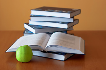 Image showing green apple and opened books on the desk