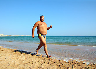 Image showing overweight man running on beach