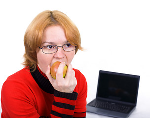 Image showing The woman bites an apple against the laptop