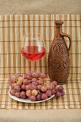 Image showing Ceramic bottle, grape and goblet on mat