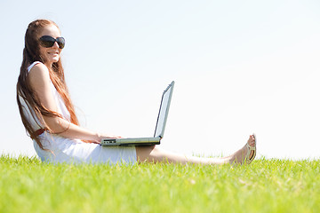 Image showing young feamle sit in the park and using a laptop