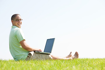 Image showing A young men sit on the in the park using a laptop