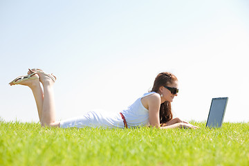 Image showing oung female lying on the grass in the park using a laptop