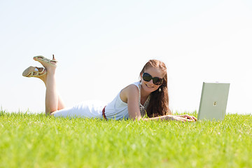 Image showing oung female lying on the grass in the park using a laptop