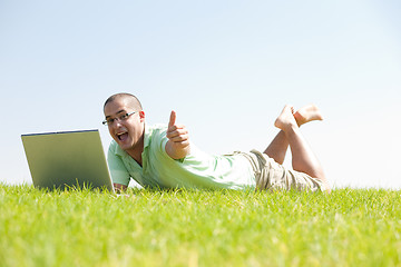 Image showing A young men sit on the in the park using a laptop