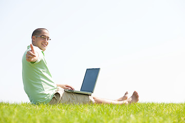 Image showing A young men sit on the in the park using a laptop